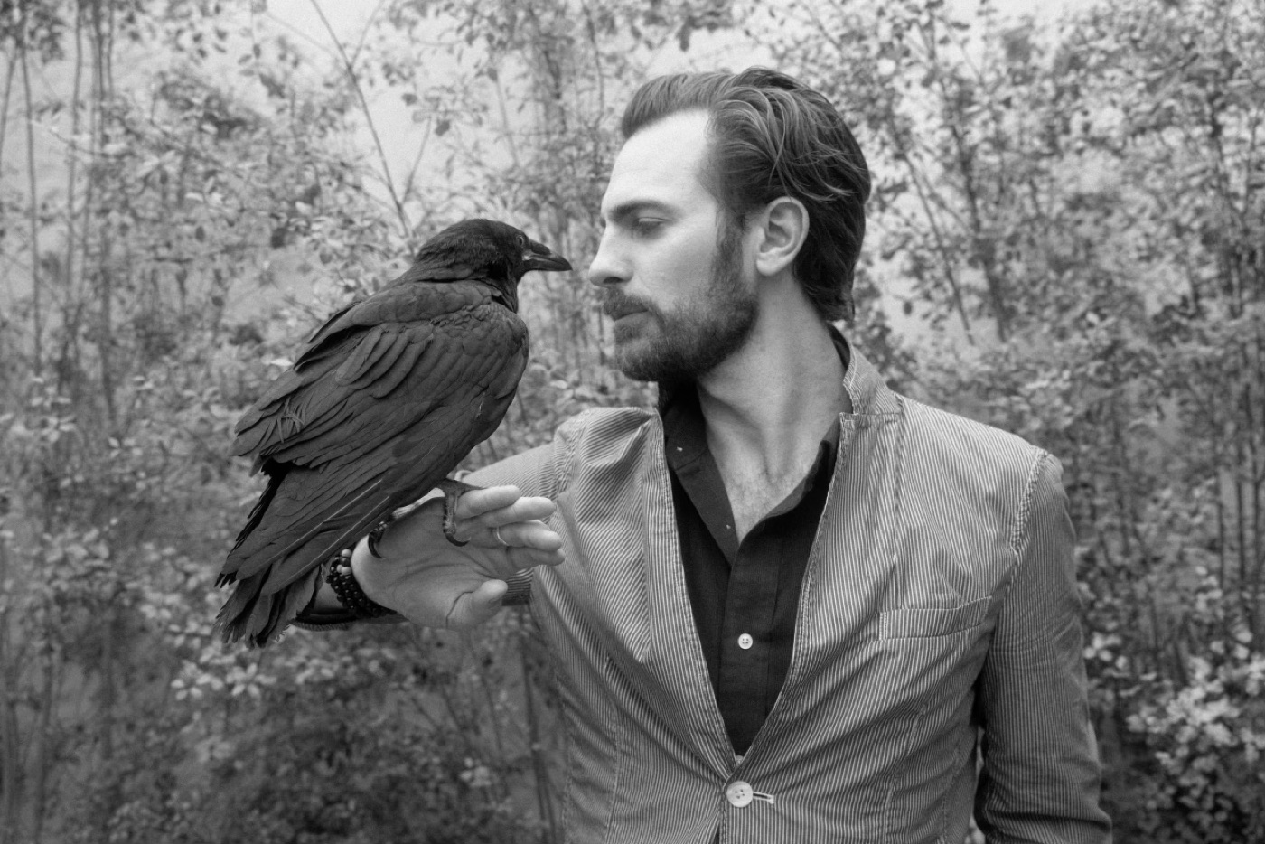 Lewis Neeff in profile, face to face with Omen, a raven perched on one hand